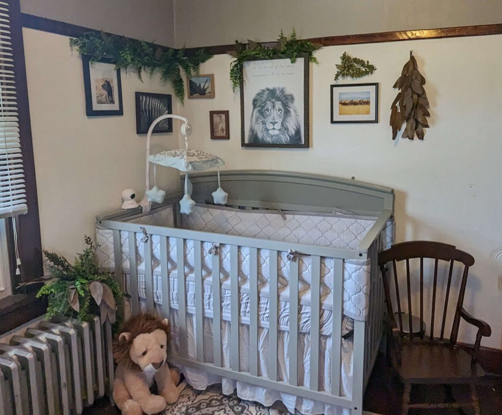 safari themed wall art for a baby room with greenery, a grey crib, stuffed lion, and child's rocking chair