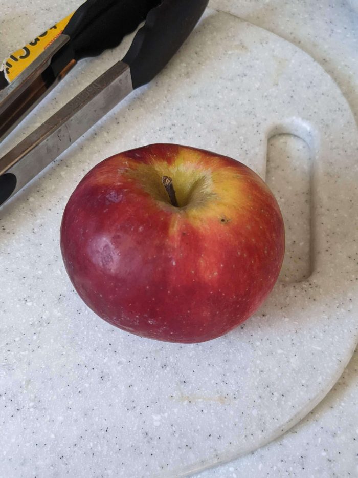 cortland apple next to tongs on a cutting board
